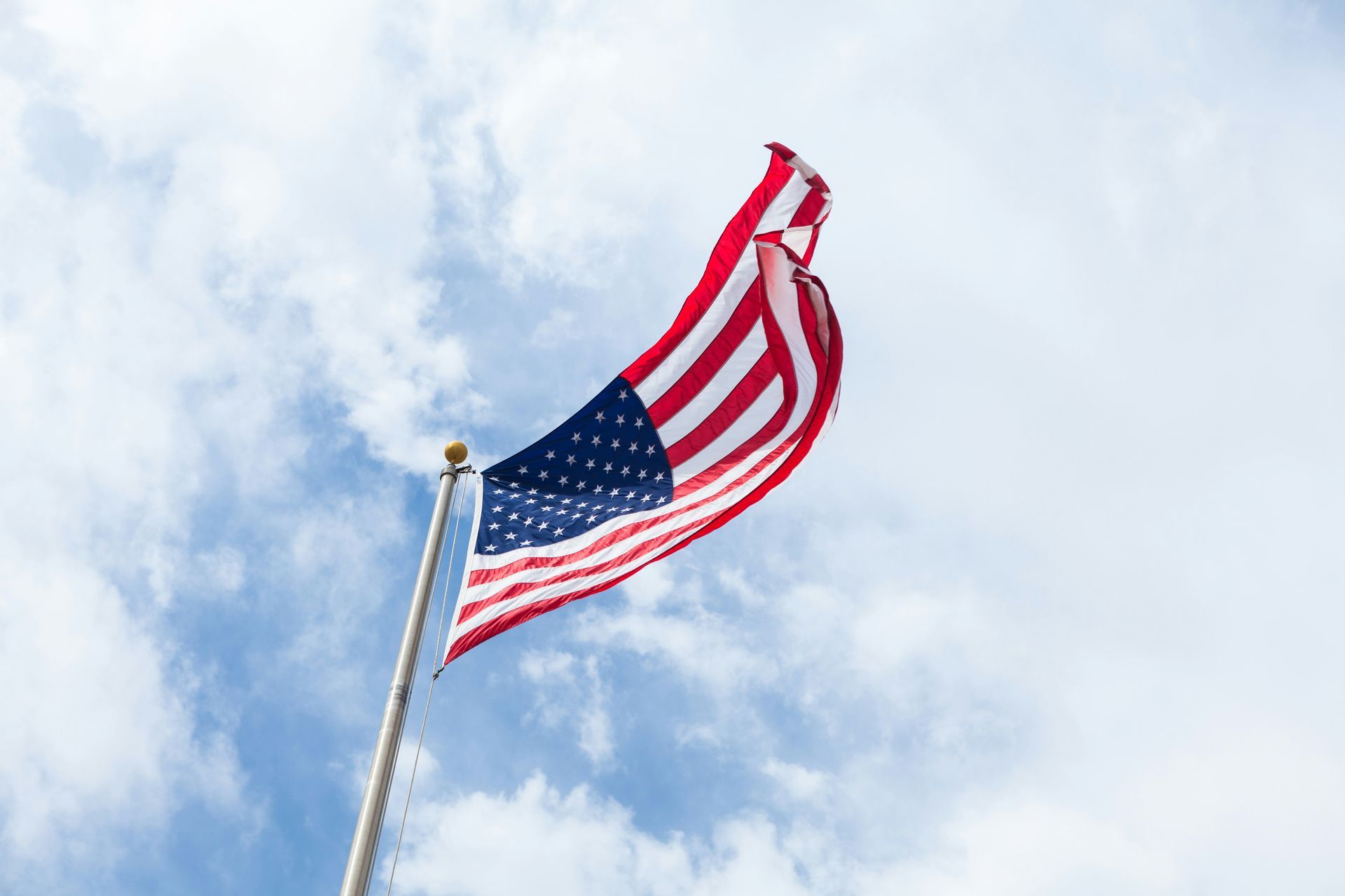 The american flag is waving in the wind against a cloudy blue sky.