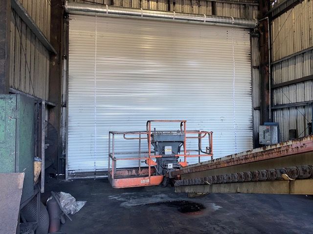 An orange lift is inside a metal building with a closed, corrugated roll-up door.