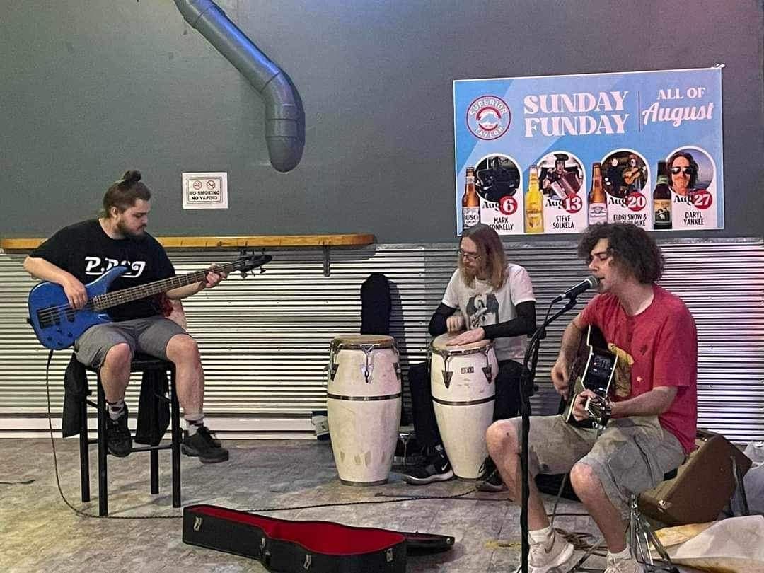 Band playing in a bar. A bassist, percussionist, and guitarist are performing.