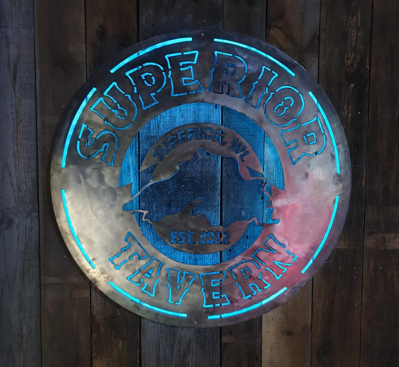 Metal sign for Superior Tavern, with backlit blue lettering, over a blue-stained wood backdrop.