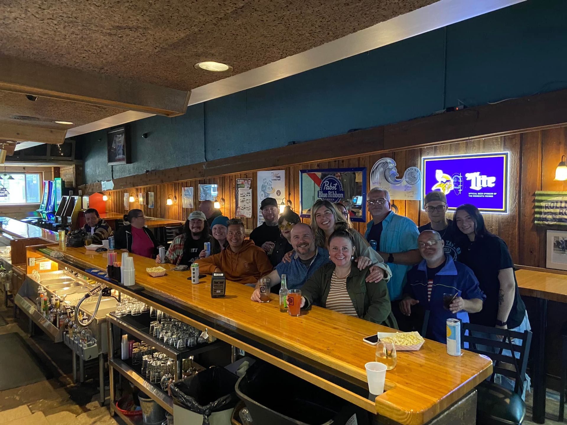 Group of people smiling at a bar, sitting at the counter. Warm lighting, wooden bar.