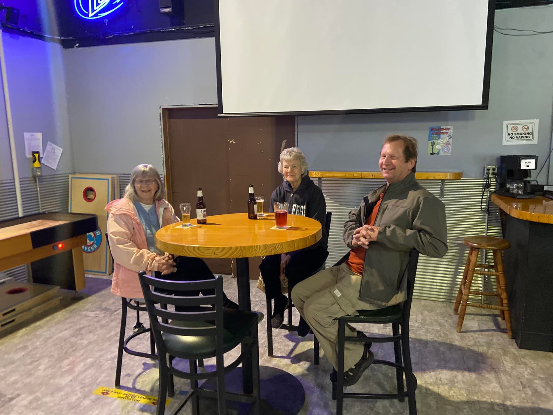Three people seated at a round table in a bar, drinks in front of them.