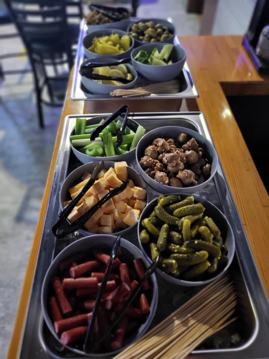 Buffet with multiple bowls of snacks: pickles, cheese, olives, celery, sausage, and mini meatballs.