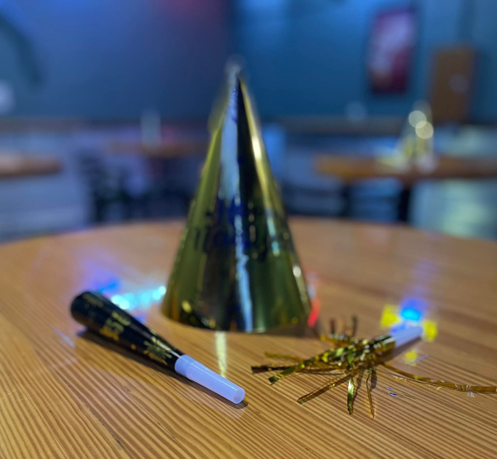 A gold party hat, noisemakers, on a wooden table. Blurred background of a room.