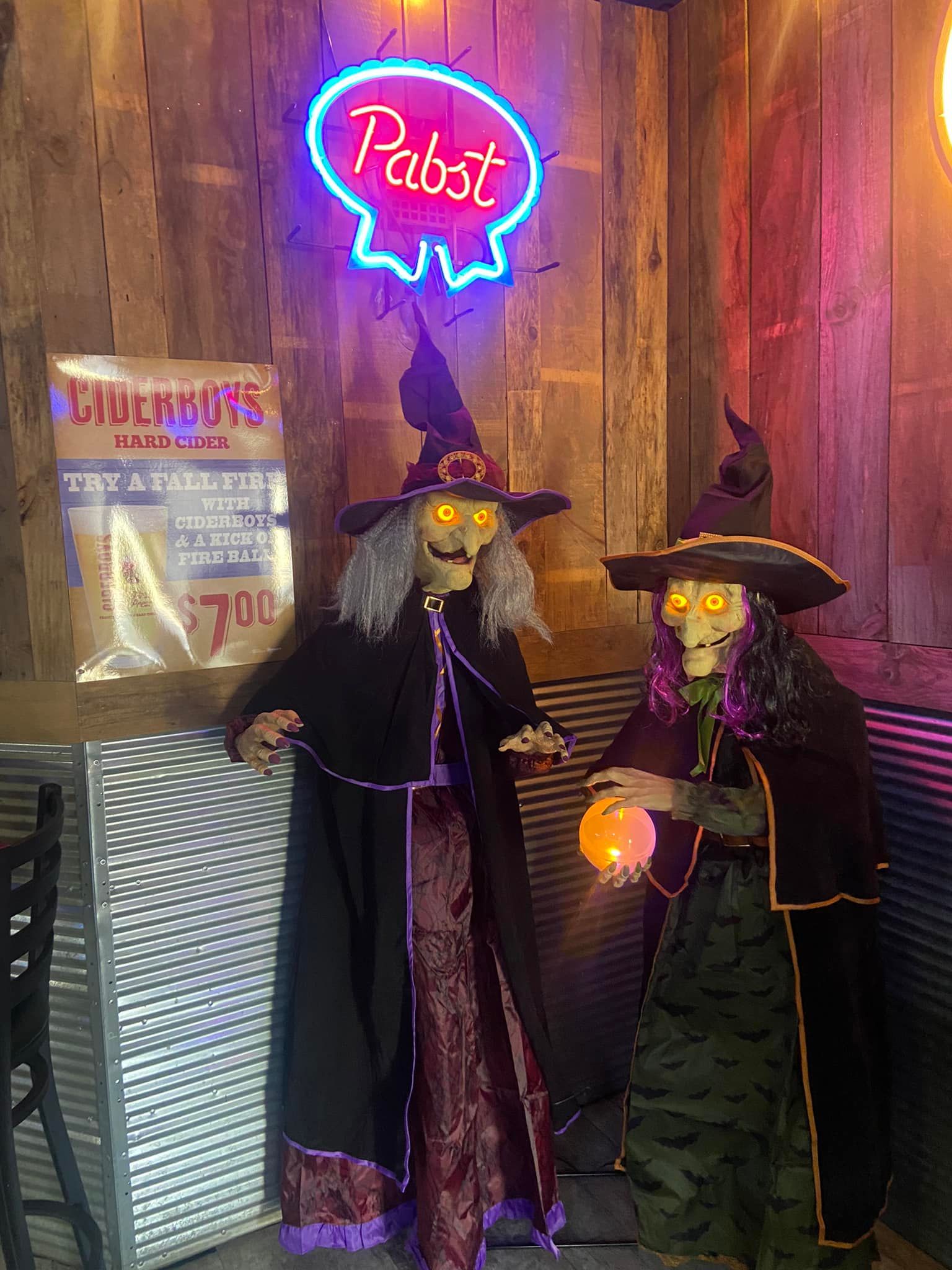 Two witch decorations with glowing eyes stand near a neon