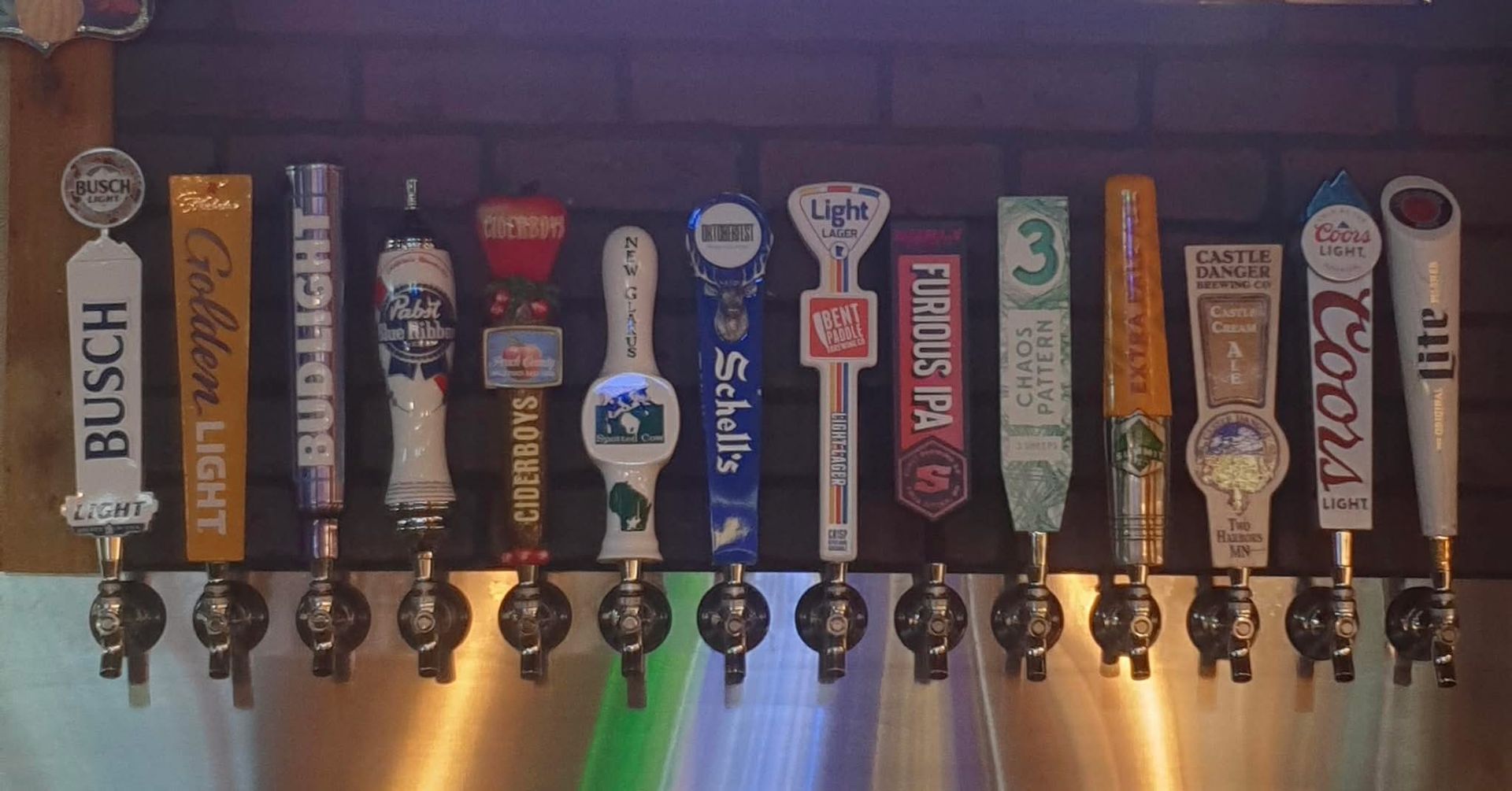 Beer taps with different brand handles, arranged in a row against a brick wall background.