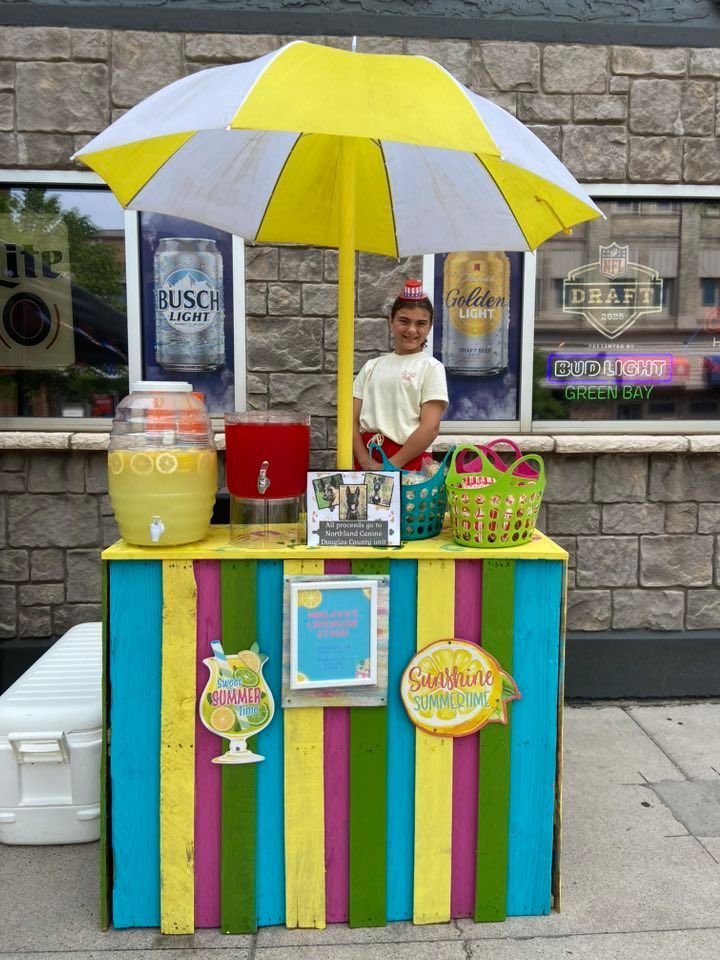 Lemonade stand with colorful stripes and a young person behind it.