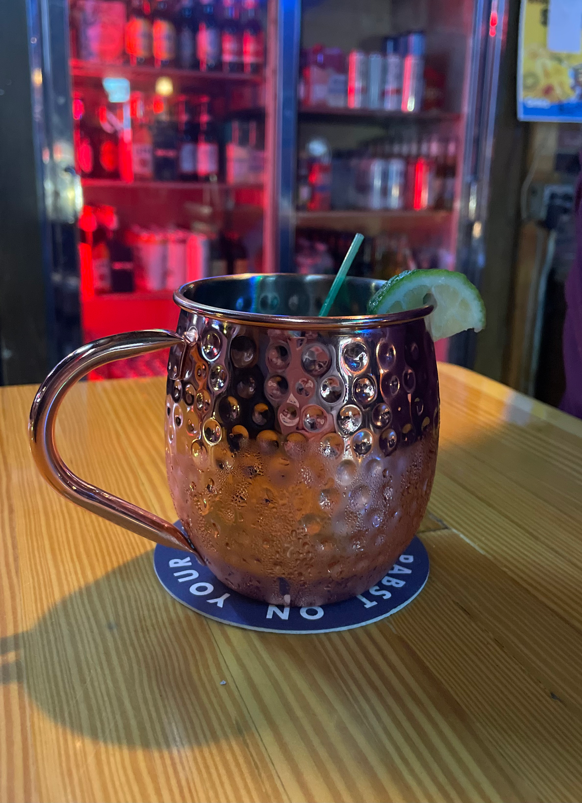 Copper Moscow Mule in a dim bar setting, with a lime garnish and straw.