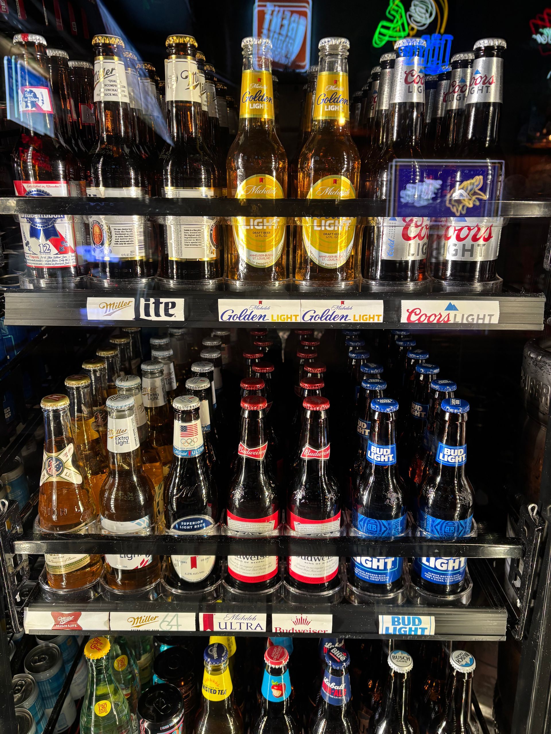 Beer bottles in a bar refrigerator; various brands and colors are visible on multiple shelves.
