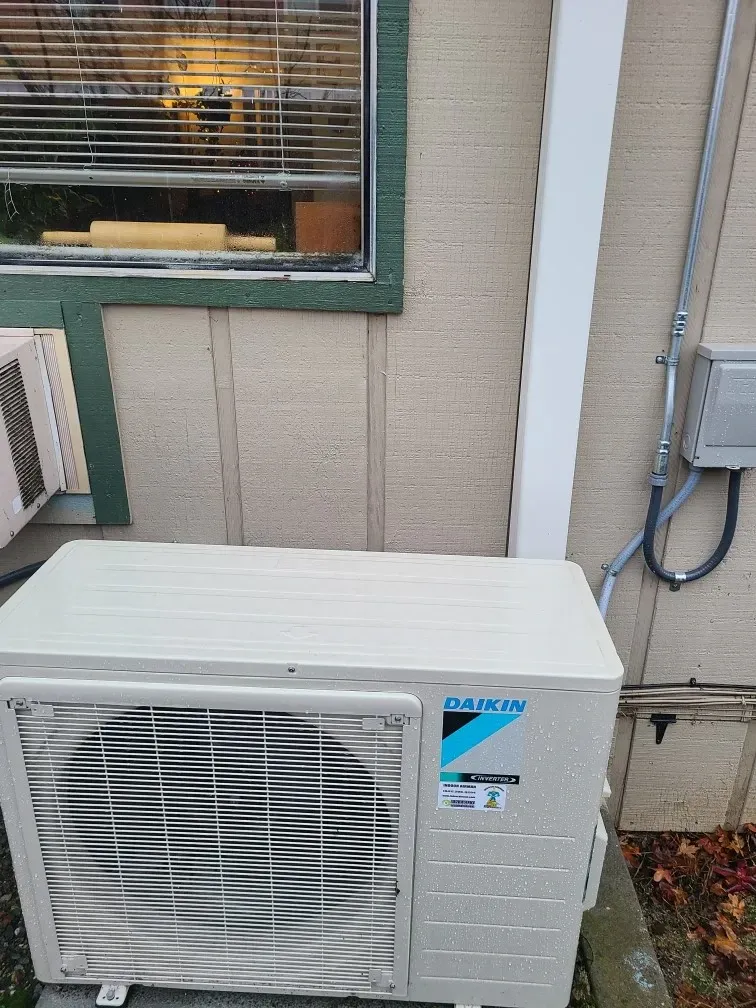 A white air conditioner is sitting outside of a building next to a window.