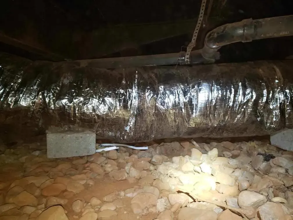 A large metal pipe is sitting on top of a pile of rocks in a basement.