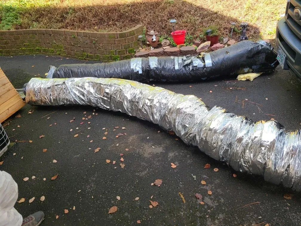A large hose wrapped in aluminum foil is laying on the ground next to a car.