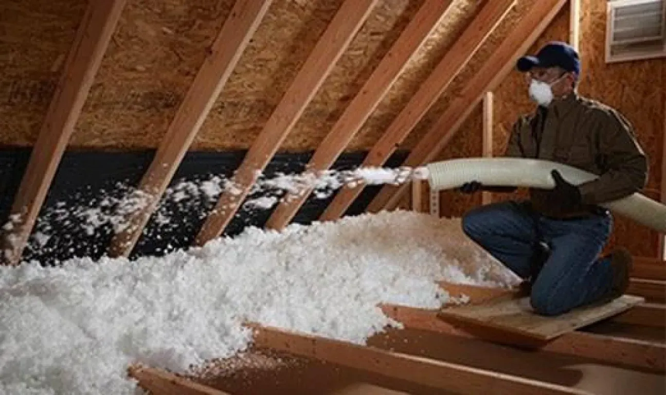 A man is blowing insulation into the attic of a house.