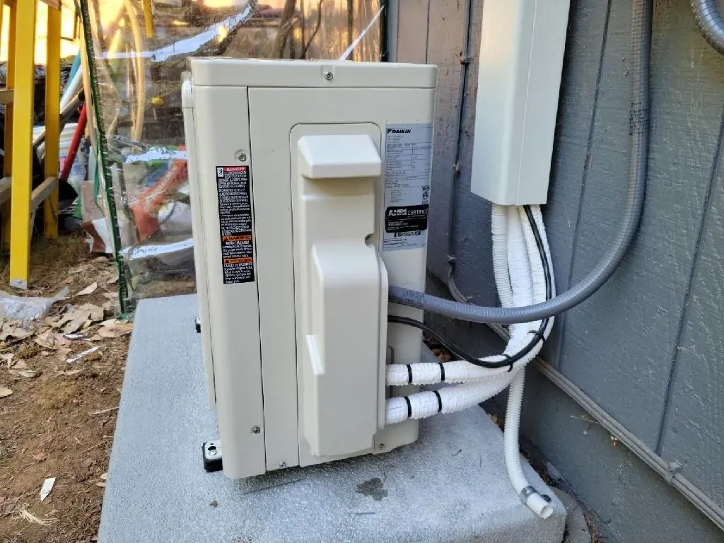A white air conditioner is sitting on the side of a building.