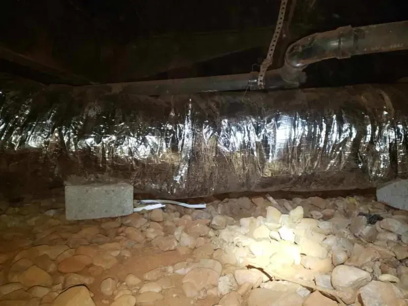 A large pipe is sitting on top of a pile of rocks in a basement.