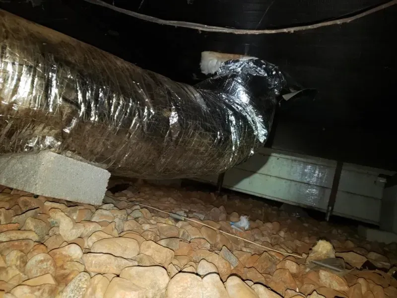 A duct is sitting on top of a pile of rocks in a basement.