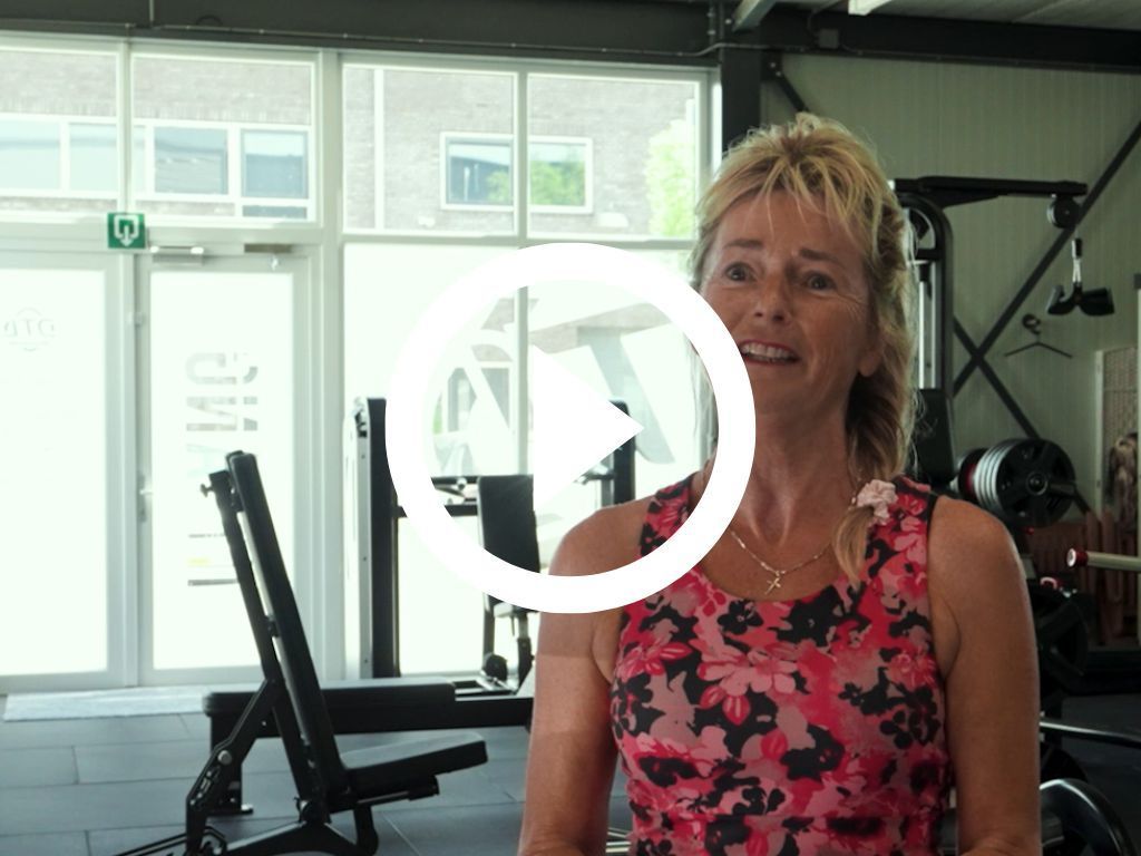 Een vrouw in een roze tanktop lacht in een sportschool.