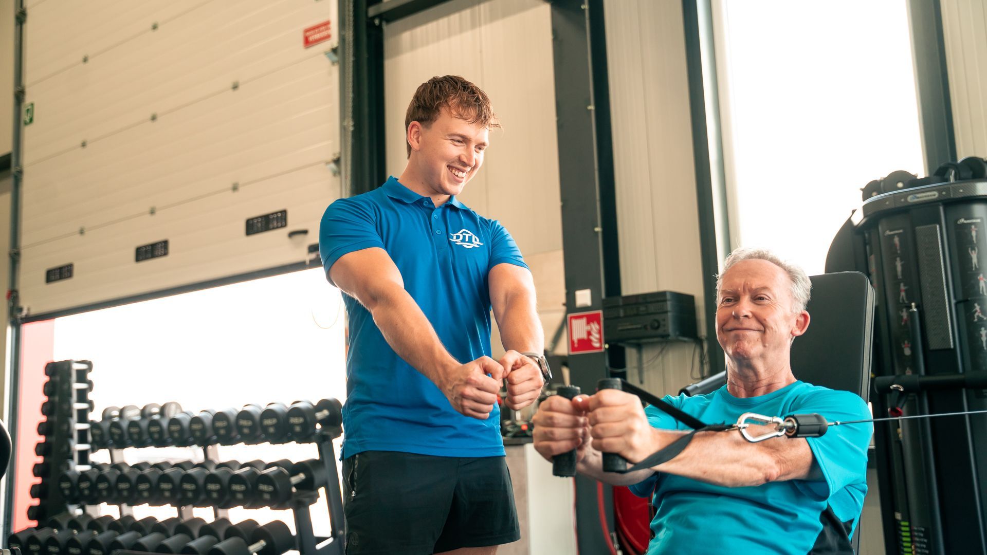 Een man helpt een oudere man met oefeningen in een sportschool.