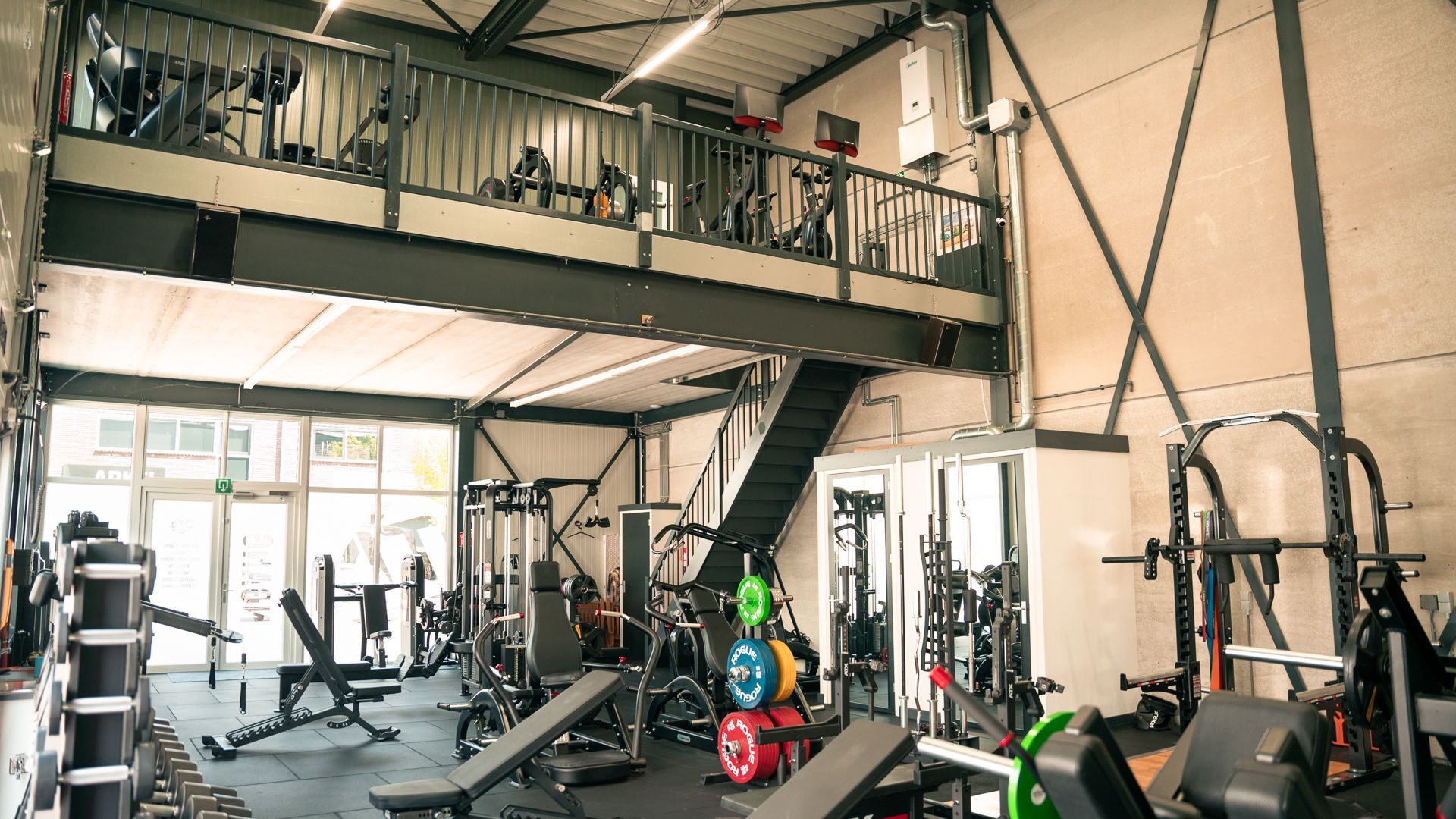 Een sportschool met veel fitnessapparatuur en een balkon.