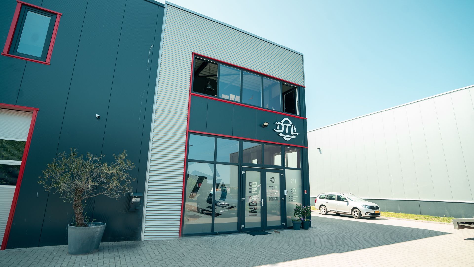 Een groot gebouw met veel ramen en auto's ervoor geparkeerd.