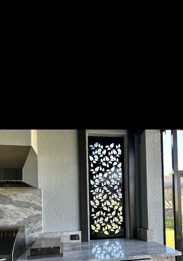A decorative black door with leaf cutouts, set in a light-colored kitchen with a granite countertop.