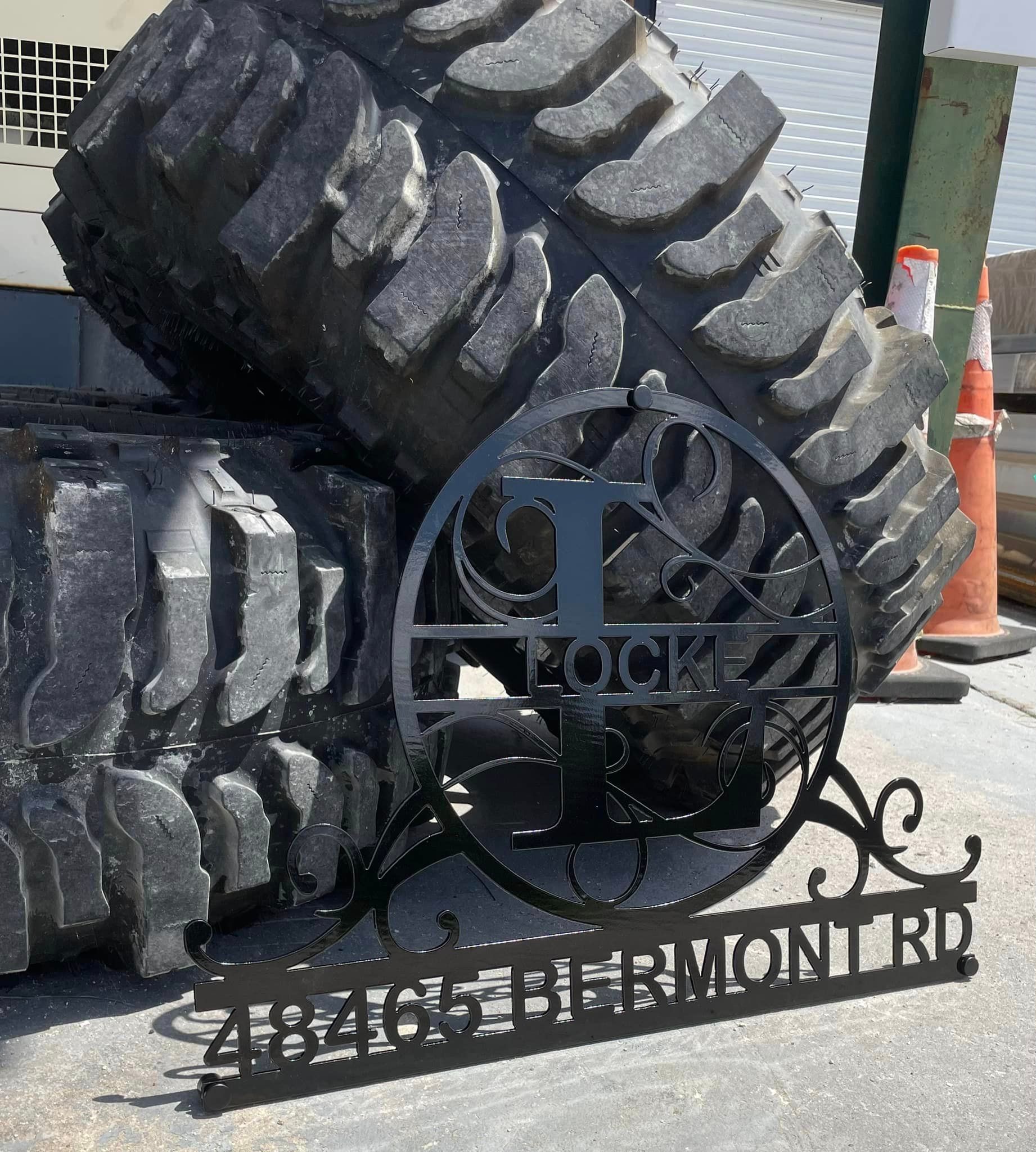 Metal address sign with a large tire in the background: 48465 BIERMONT RD. A stylized 