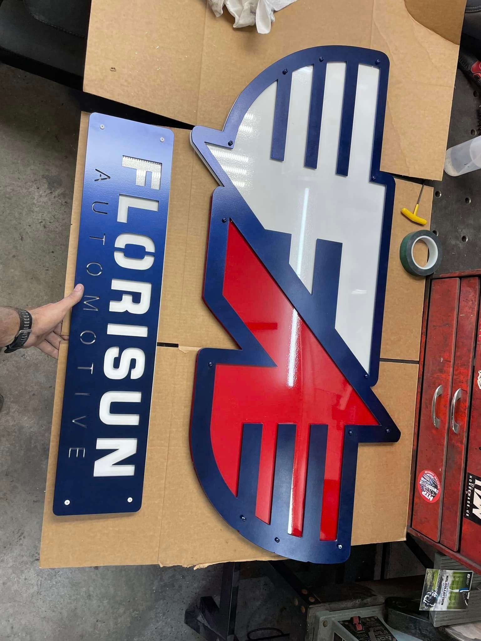 Blue, white, and red Florisun Automotive sign on a cardboard box with a person's hand on the side.