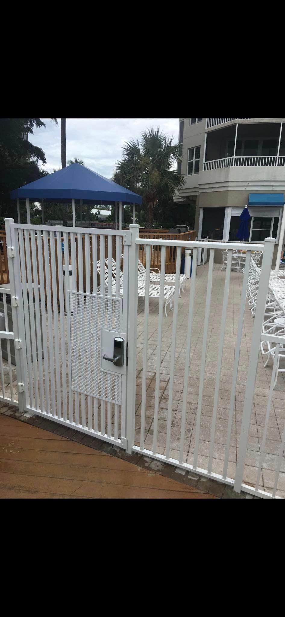 White fence with a gate in front of a blue gazebo and building.