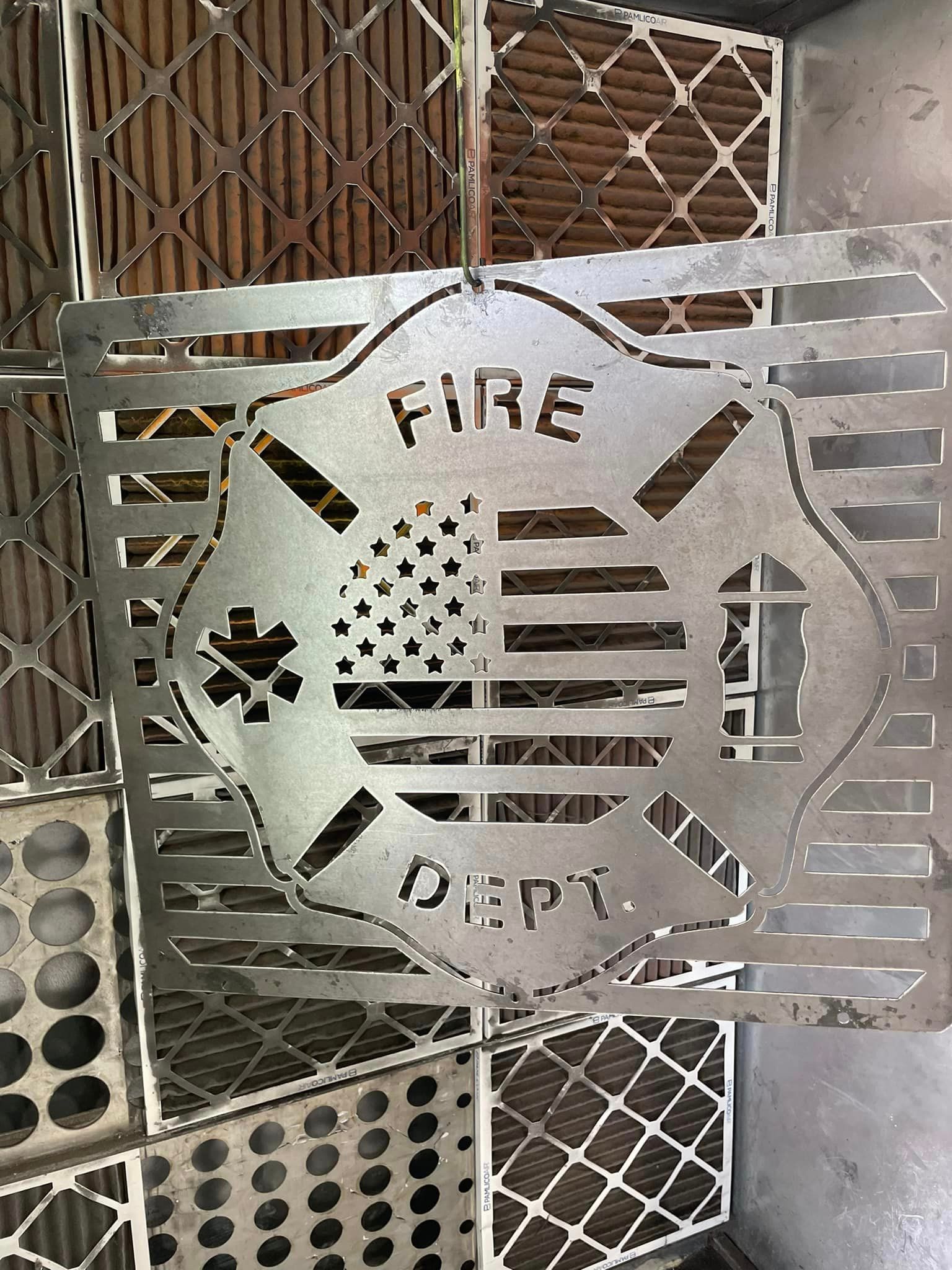 Metal grate with a firefighter emblem, cut with “FIRE DEPT.”, an American flag, and a medical symbol.