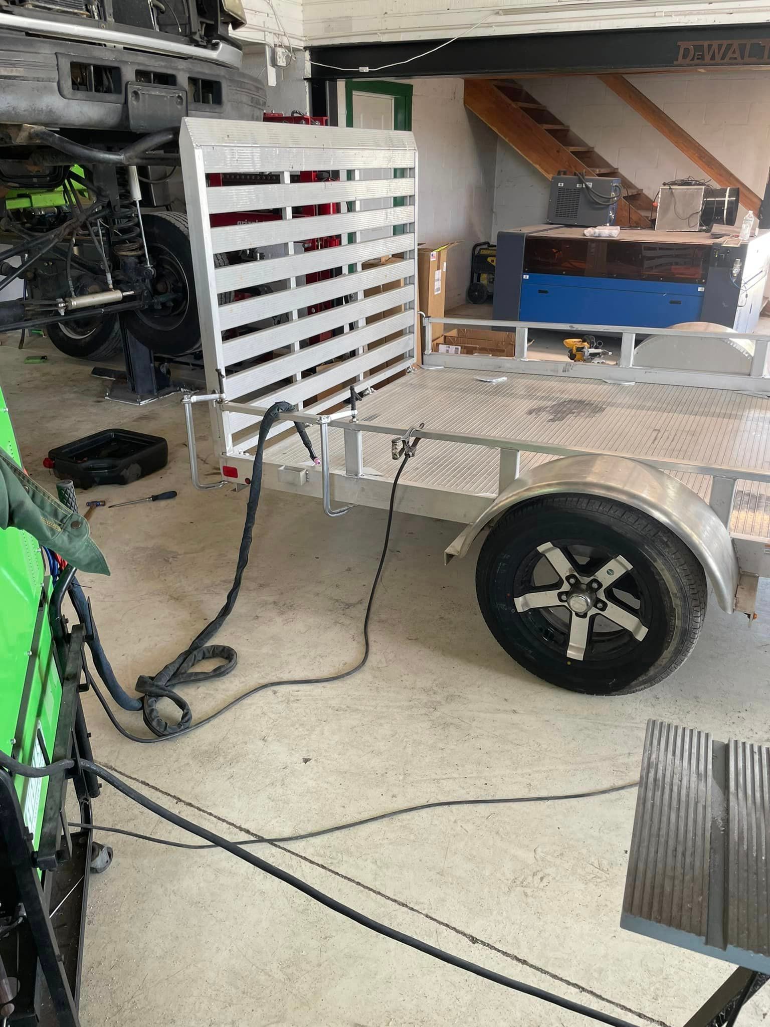 An aluminum trailer with a ramp inside a garage. A black cable is connected to the trailer.