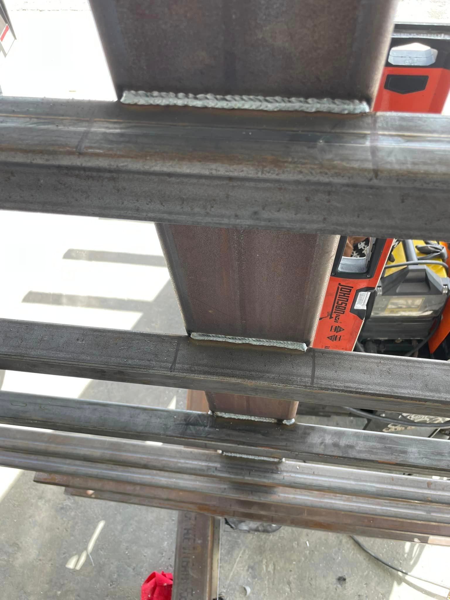 Steel beams welded together, forming a support structure. Welds appear to be done outdoors.