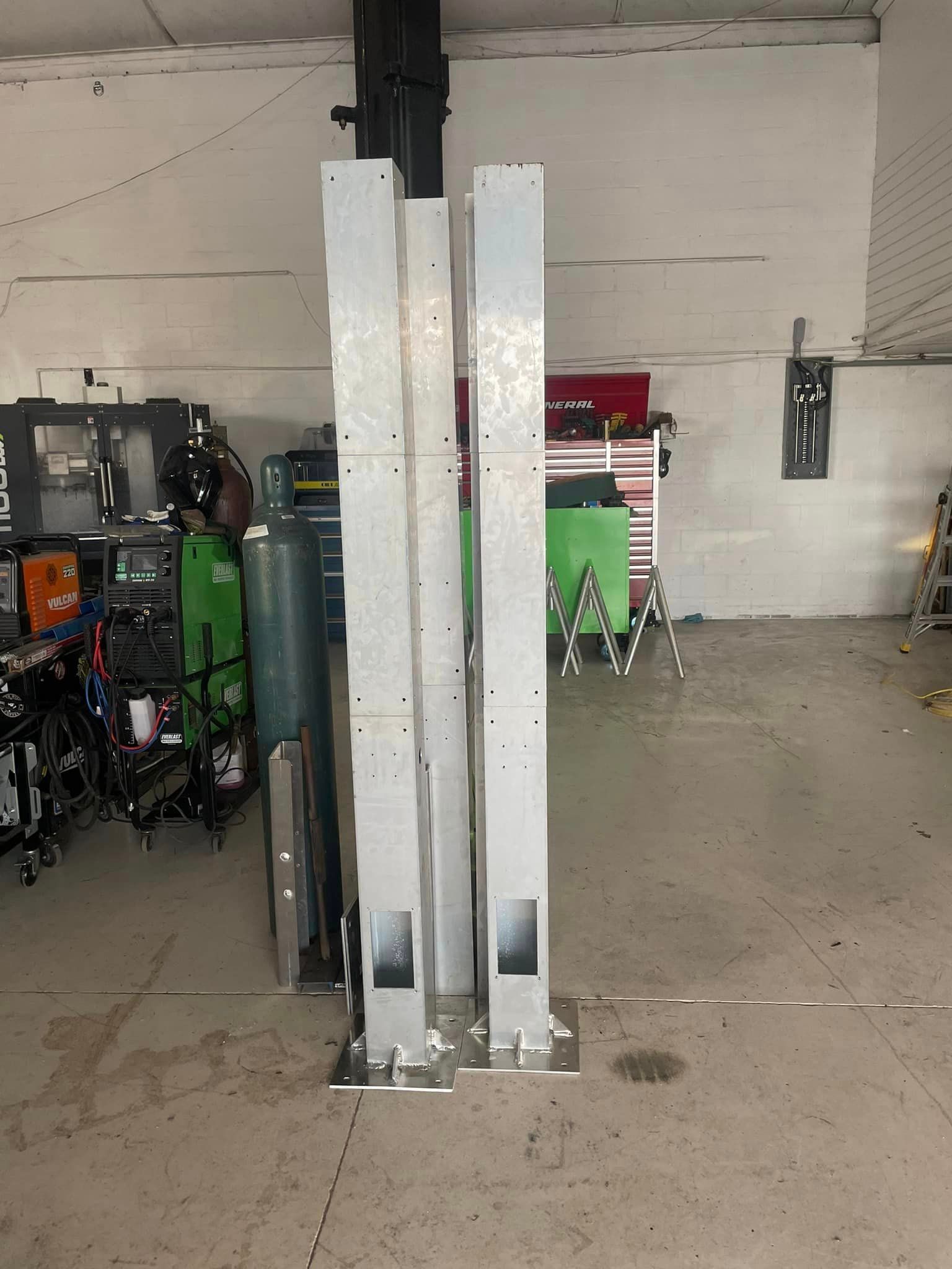 Three silver car lift columns standing on a garage floor.