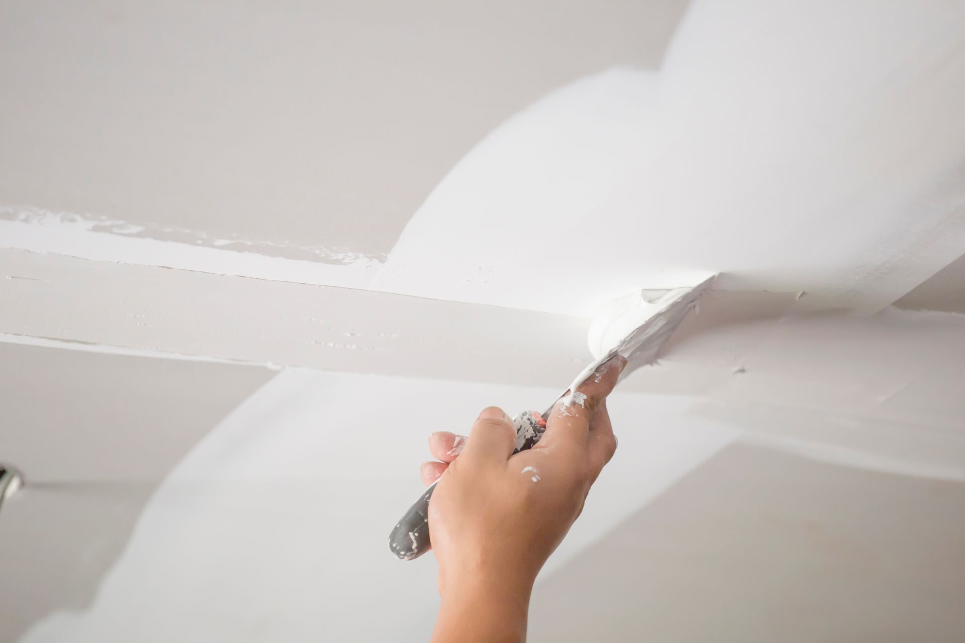 Hand smoothing white joint compound on a ceiling seam with a putty knife