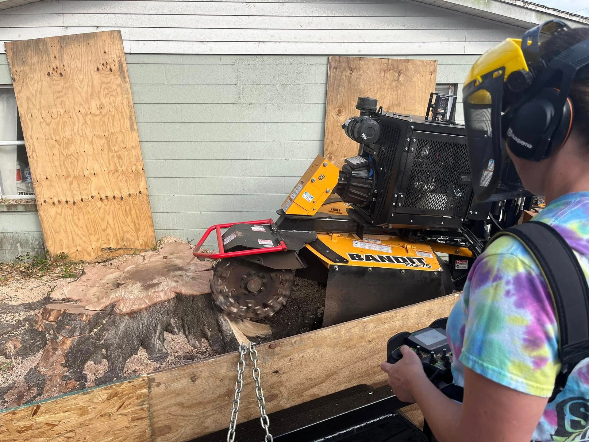 A person wearing headphones is standing next to a stump grinder.