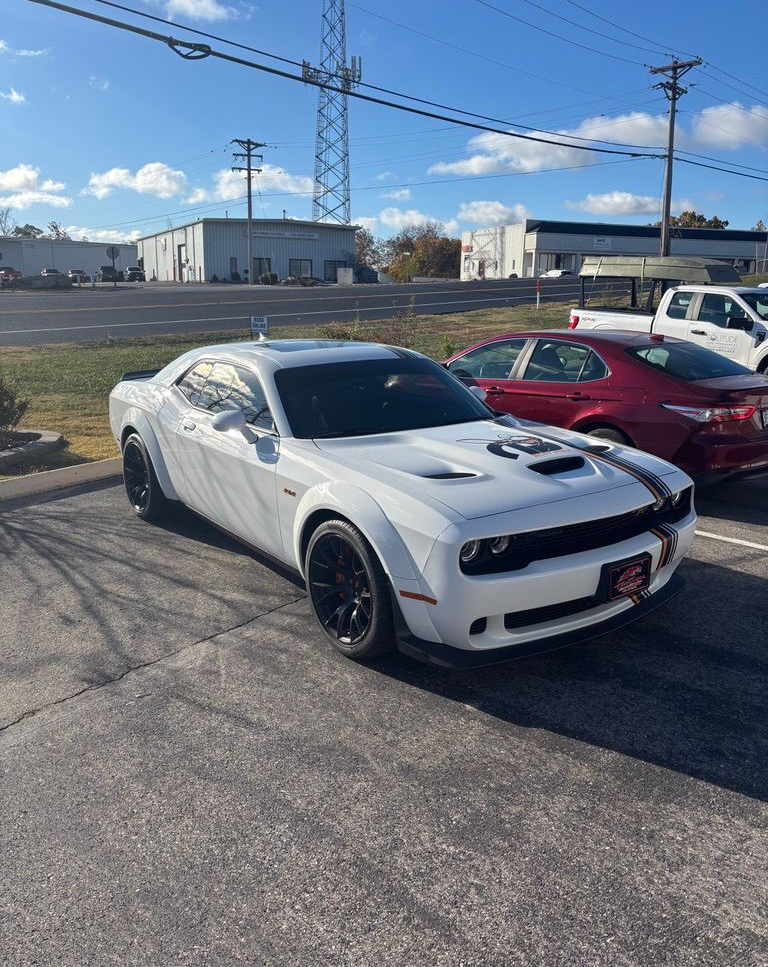A white Dodge Challenger widebody parked in a sunny lot, with a red sedan parked behind it.