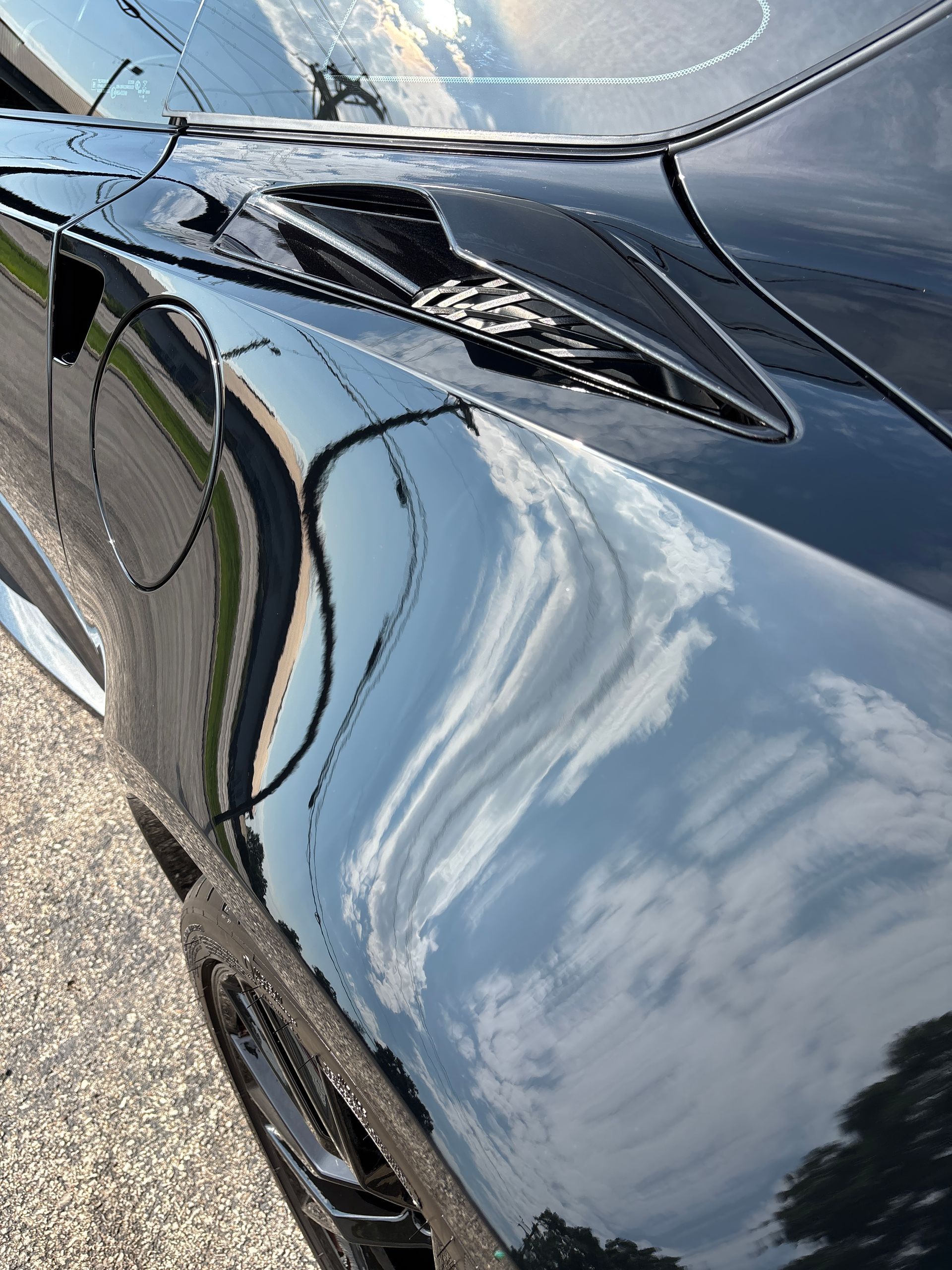 Black sports car with reflections of clouds and sky.