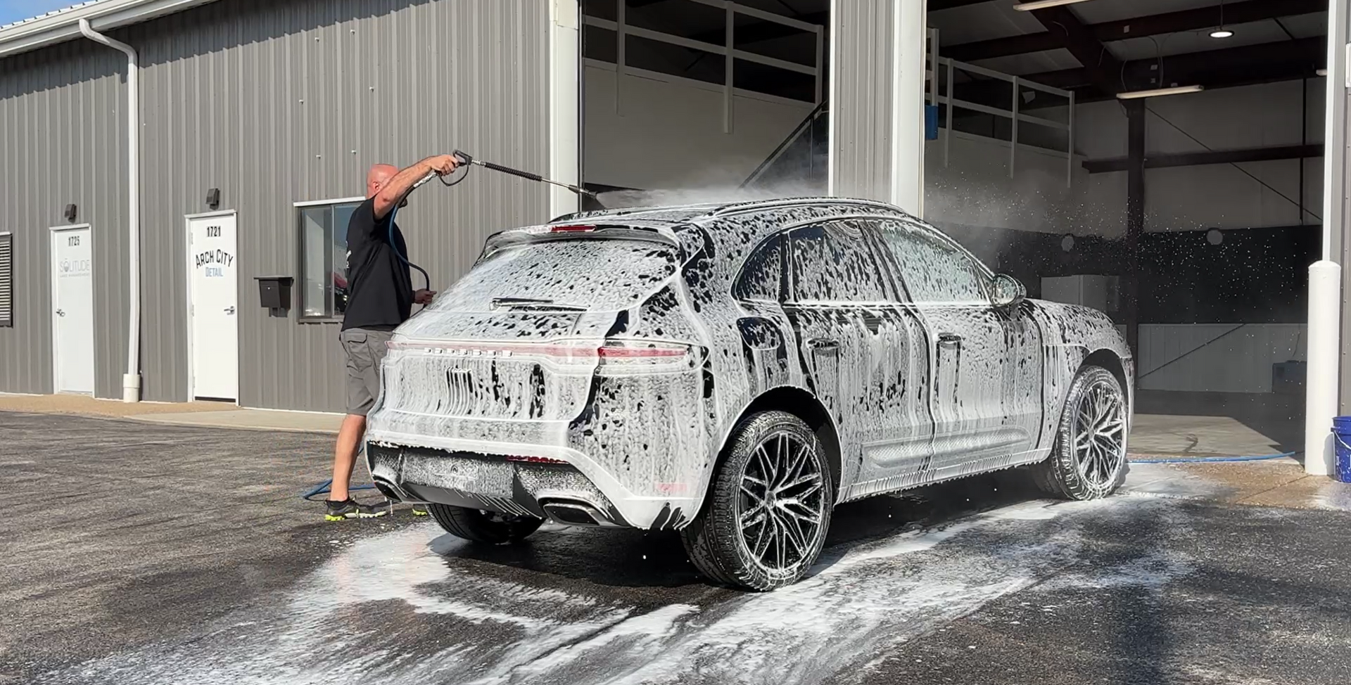 Person washing a black SUV with soap at a car wash.