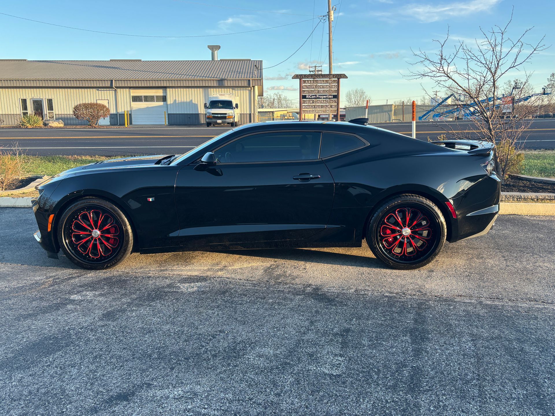 Black Chevrolet Camaro with red rims parked outdoors on pavement.