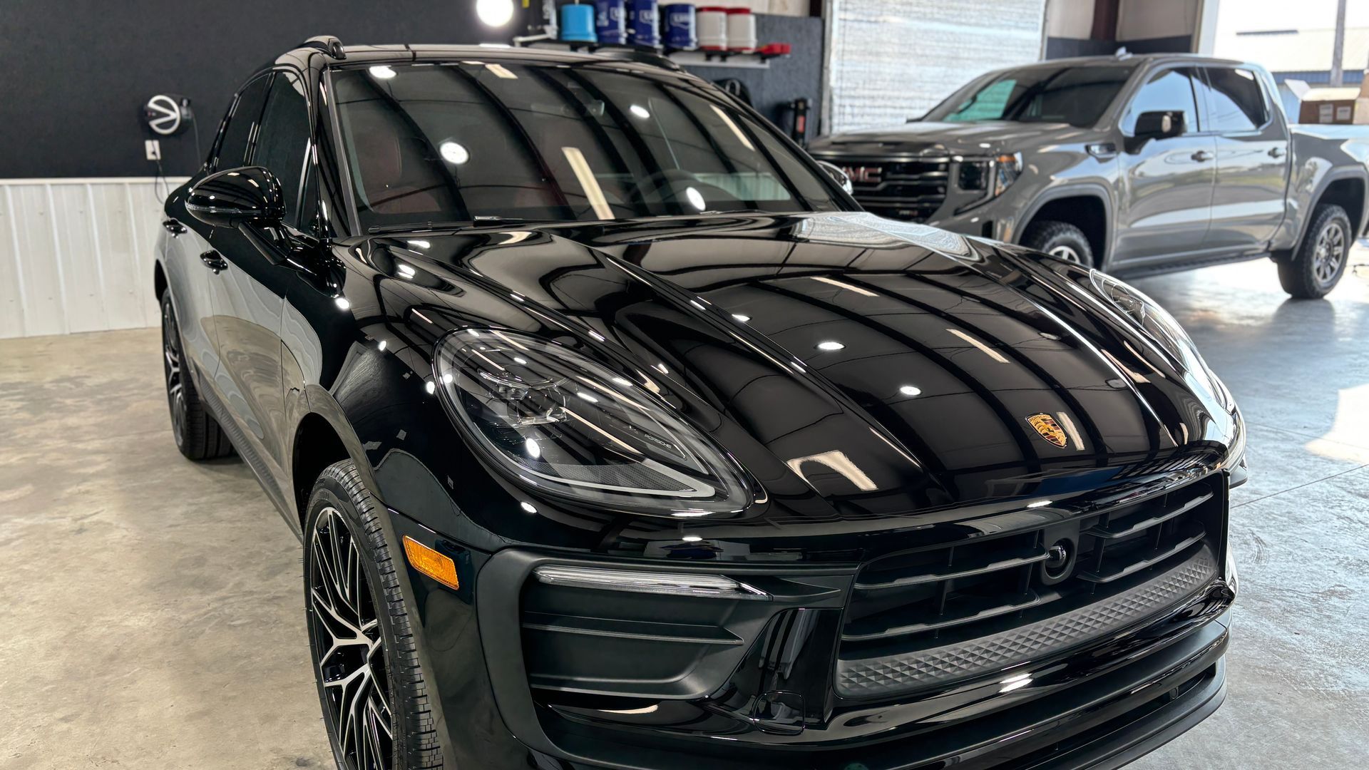 Black Porsche SUV parked inside a garage. Reflective black paint, sleek design. Another car visible in the background.