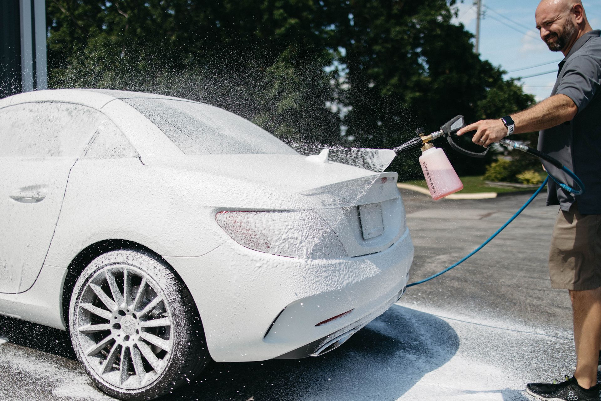 Man washing a white car with foamy soap outdoors.