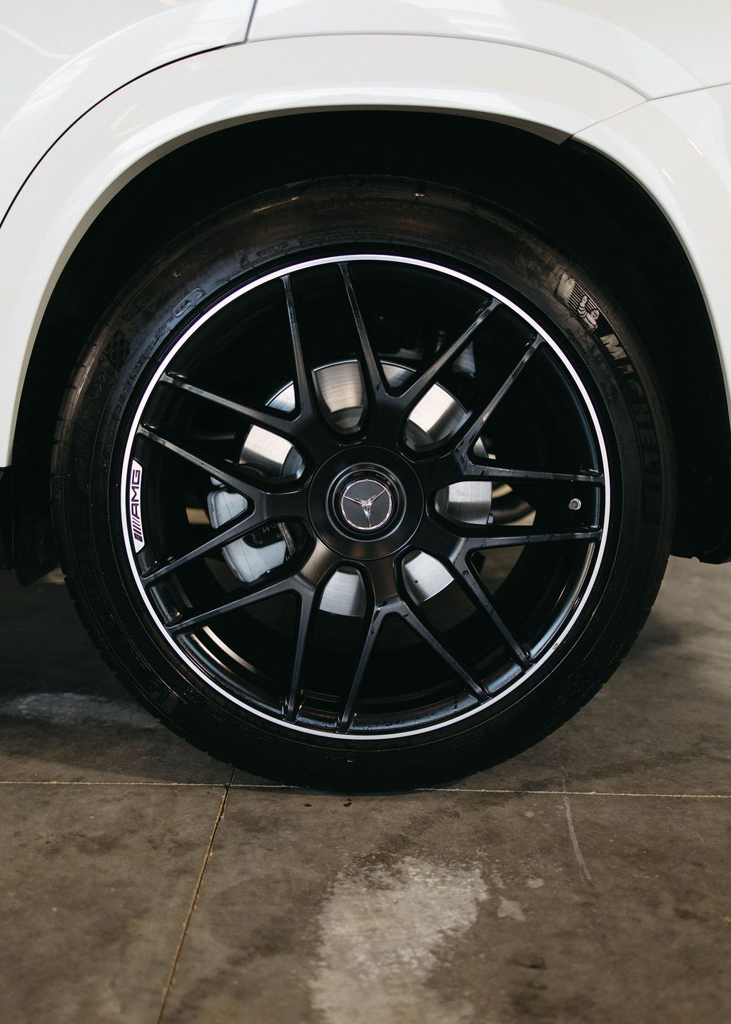Black Mercedes-Benz car wheel with black and white rim against white car body.