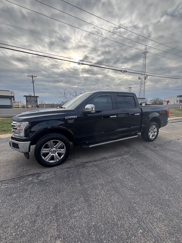 Black Ford F-150 pickup truck parked on asphalt under a cloudy sky. Chrome accents, side steps.
