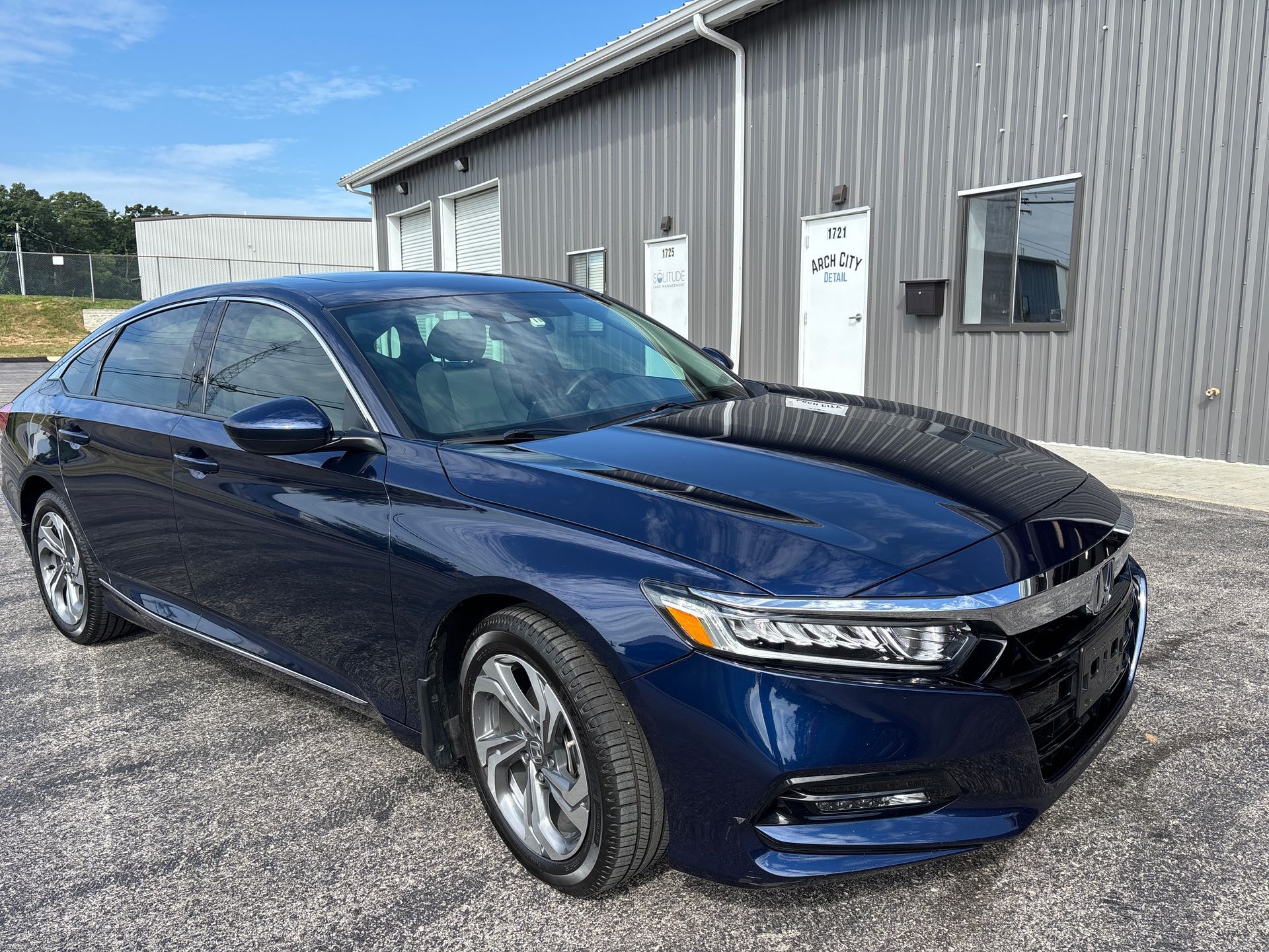 Blue Honda Accord parked in front of a gray building on a sunny day.