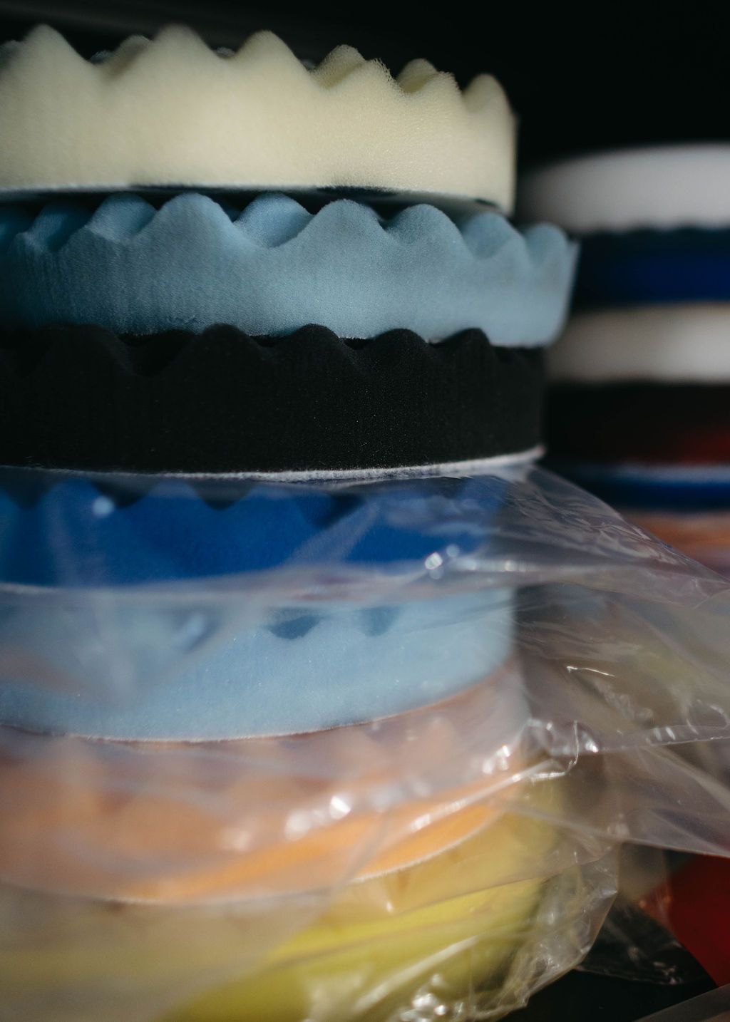 Stack of colorful, textured buffing pads in a storage area, varying shades of blue, black, and orange.