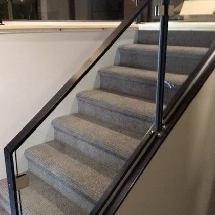 Staircase with gray carpeted steps and glass and black metal railing.