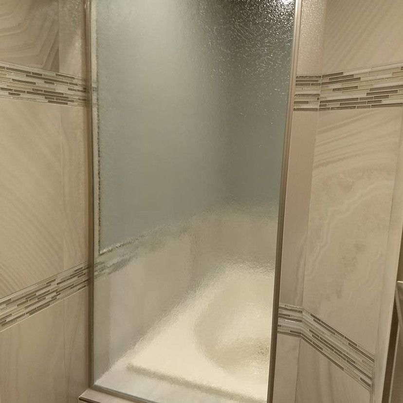 Shower with frosted glass panel and neutral tile surround.
