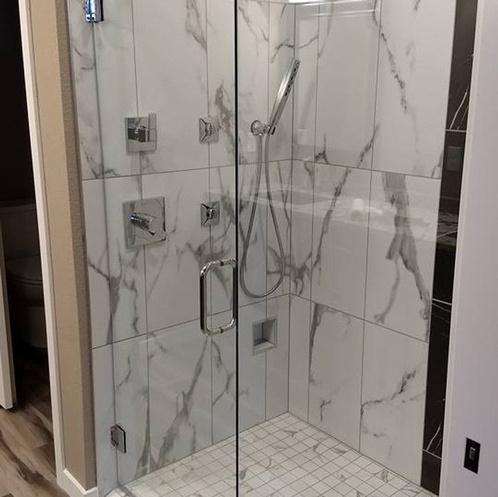 Glass-enclosed shower with white and gray marble-look tile, chrome fixtures, and a glass door.