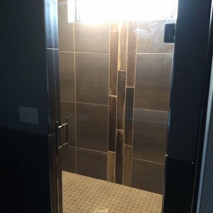 Shower stall with dark brown tile and decorative vertical wood-look accents. Glass door and small window.