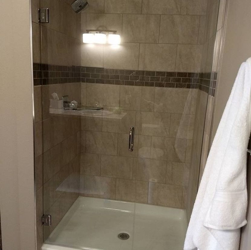Glass-enclosed shower with beige tile, recessed shelf, and a white robe hanging to the side.