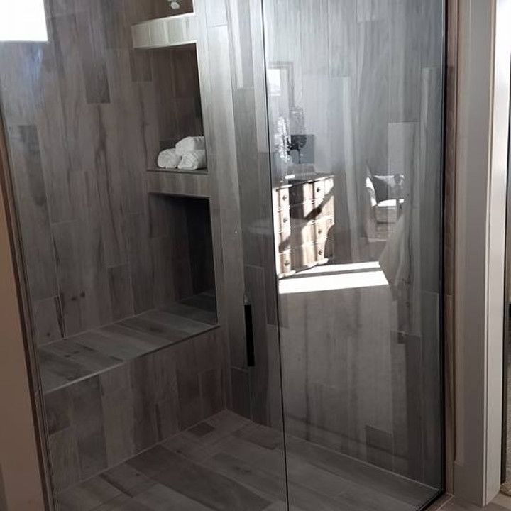 Shower with wood-look tile, built-in bench, and glass door. Includes recessed storage niche and visible sink area.